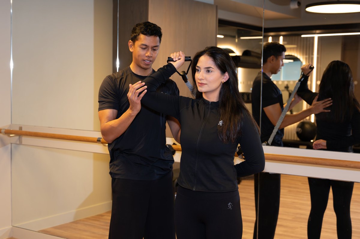 Joel Nathan coaching a resistance band shoulder exercise in the gym