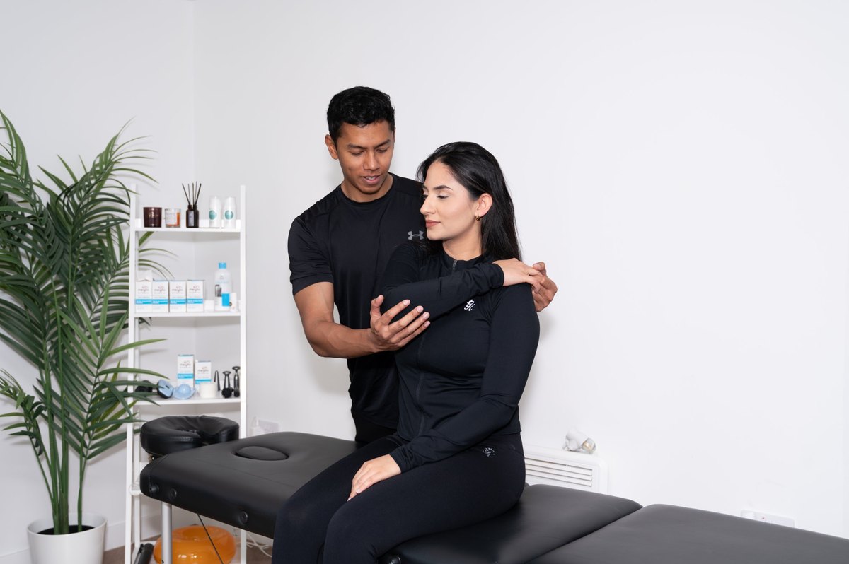 Joel Nathan assessing a patient's shoulder mobility with an arm raised behind the back