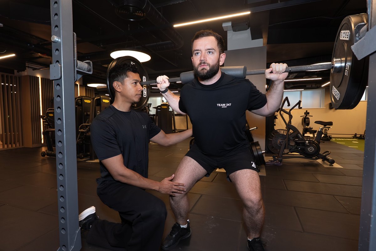 Joel Nathan coaching a patient through a barbell squat in the gym